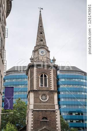 Historic Church Tower with Weathered Stone Spire and Antique Clock Set Against Modern Glass Office Building in Central London, Highlighting Contrast Between Old and New Urban Forms. Historic Church Tower with Weathered Stone Spire and Antique Clock Set Against Modern Glass Office Building in Central London, Highlighting Contrast Between Old and New Urban Forms. 126143661