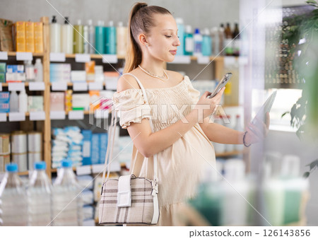 Young pregnant woman in pharmacy scans QR code on soothing body balm Young pregnant woman in pharmacy scans QR code on soothing body balm 126143856
