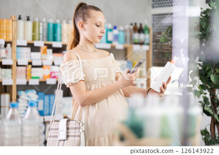 Young pregnant woman in pharmacy scans QR code on soothing body balm Young pregnant woman in pharmacy scans QR code on soothing body balm 126143922