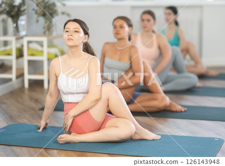 Young girl sitting in twisting asana Matsyendrasana at yoga class Young girl sitting in twisting asana Matsyendrasana at yoga class 126143948