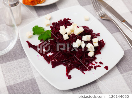 On plate is portion of salad of grated boiled beetroot with addition of small pieces of white cheese. On plate is portion of salad of grated boiled beetroot with addition of small pieces of white cheese. 126144060