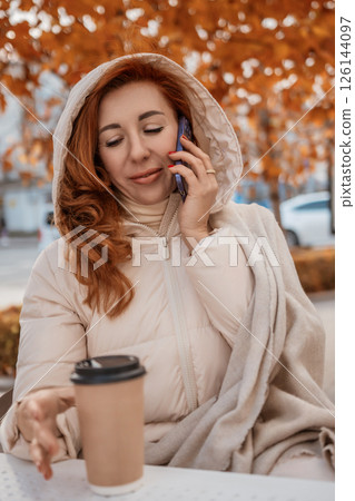 Woman Autumn Park PhoneCall: Redhead enjoys coffee, phone conversation outdoors during fall. 126144097