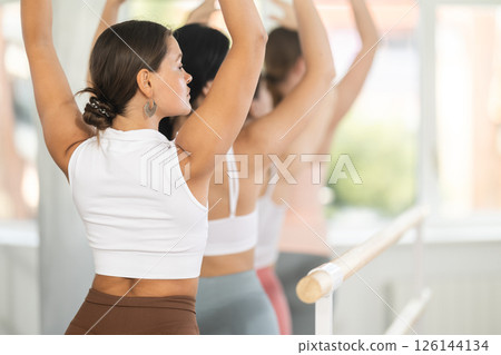 Young girl practicing fifth arm position holding by ballet barre 126144134