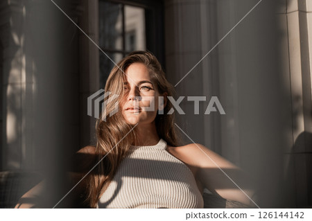 Woman Portrait Sun Light Window - Young woman in a white top posing for a portrait in front of a window with sunlight streaming through. 126144142
