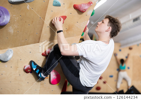 Teenage boy climbs steep artificial wall in sports complex and trains endurance Teenage boy climbs steep artificial wall in sports complex and trains endurance 126144234