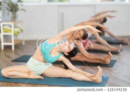 Girl teaches yoga lesson, shows students technique of performing Parivritta Janu Shirshasana asana 126144236