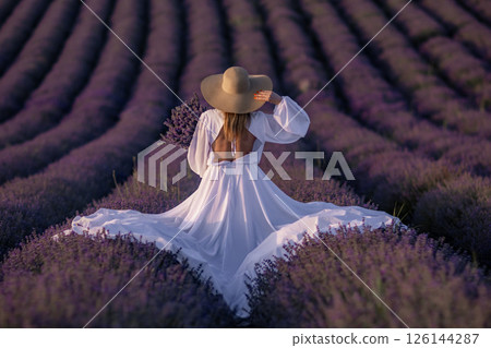 Lavender Fields Provence Woman; Sunset photoshoot: Elegant woman in white dress enjoys picturesque Provence lavender fields during golden hour. Lavender Fields Provence Woman; Sunset photoshoot: Elegant woman in white dress enjoys picturesque Provence lavender fields during golden hour. 126144287
