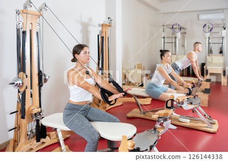Sportive young girl training her arms pulling handle of cable exercise machine 126144338