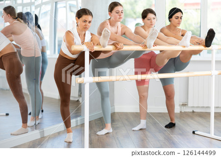 Group of young female ballet students stretching at barre Group of young female ballet students stretching at barre 126144499