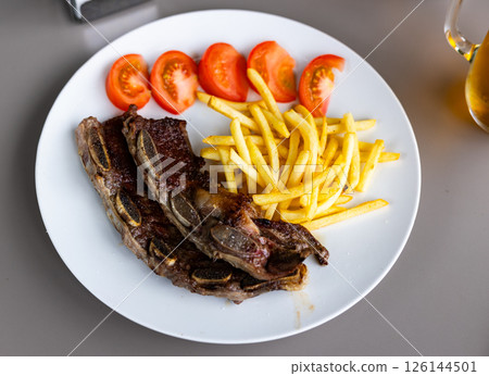 Spanish cuisine. Grilled beef ribs with a side dish of fresh tomatoes and fried potatoes Spanish cuisine. Grilled beef ribs with a side dish of fresh tomatoes and fried potatoes 126144501