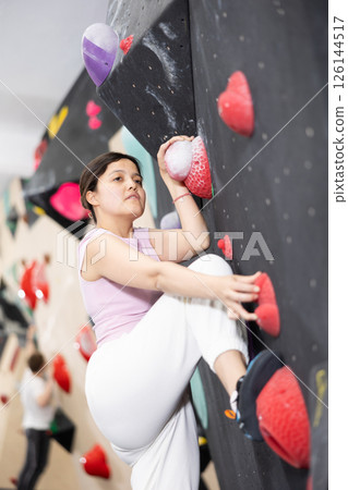 Young Asian woman climbs steep artificial wall in sports complex and trains endurance Young Asian woman climbs steep artificial wall in sports complex and trains endurance 126144517