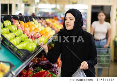 Young asian woman in hijab chooses quality juicy ripe apples Young asian woman in hijab chooses quality juicy ripe apples 126144542