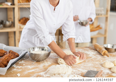 Cute doughs arranged on table in bakery with close-up of woman's hands skillfully kneading dough at food production line 126144597