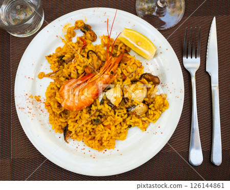 Paella made of rice and different seafood served in plate with table appointments 126144861