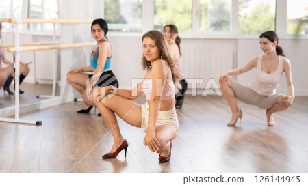 Girls perform dance in heels, squat down, actively repeat movements of instructor. 126144945