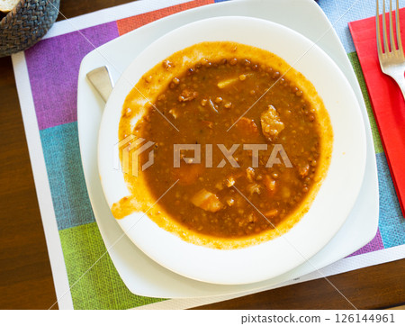 Spicy stewed lentils with suasage and vegetables with thick tomato sauce served in white plate. Spanish cuisine 126144961