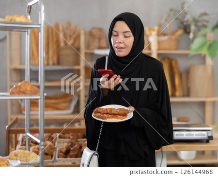 European Muslim girl customer holds pastry on disposable plate and recognizes it using app 126144968