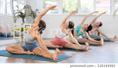 Women exercising Hatha yoga in fitness studio, sitting on mat and doing stretching in Parivrtta Janu Sirsasana 126144993
