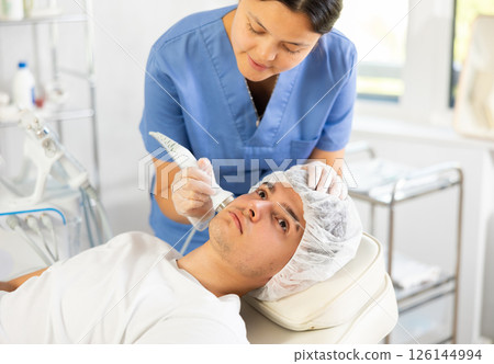 Young woman cosmetologist doing ultrasound procedure to young man 126144994