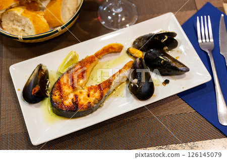 Piece of fried salmon is served on rectangular plate, and decorated with mussels. Piece of fried salmon is served on rectangular plate, and decorated with mussels. 126145079