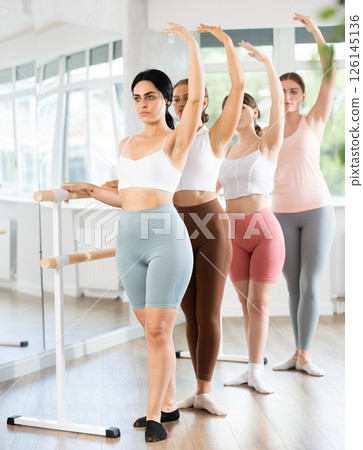 Young girl practicing third position holding by ballet barre Young girl practicing third position holding by ballet barre 126145136