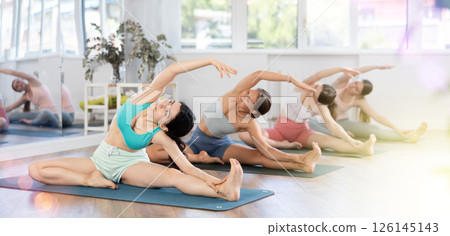 Girl teaches yoga lesson, shows students technique of performing Parivritta Janu Shirshasana asana Girl teaches yoga lesson, shows students technique of performing Parivritta Janu Shirshasana asana 126145143