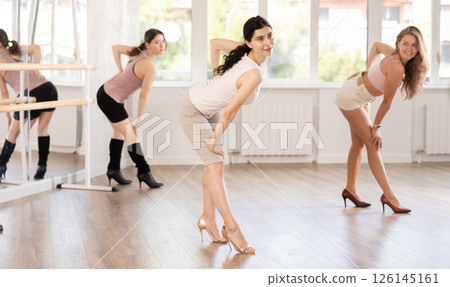 Graceful women blending sensuality with fashion while partaking in group high heels dance class Graceful women blending sensuality with fashion while partaking in group high heels dance class 126145161