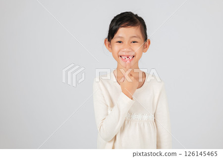 Schoolgirl pointing at her tooth gap, smiling brightly. The dentist educates on the natural process of tooth loss and how the new tooth gap affects dental development. isolated white background 126145465
