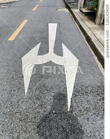 A road marking shows an arrow with split direction, indicating two possible routes and forward direction, it represent anticipation A road marking shows an arrow with split direction, indicating two possible routes and forward direction, it represent anticipation 126145609