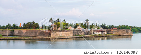 The Mannar Dutch Fort in Sri Lanka stands proudly along the calm waterfront, its weathered stone walls and colonial architecture surrounded by lush palms and a serene sky 126146098