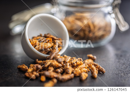 Dried salted insect. Roasted crickets on black table. 126147045