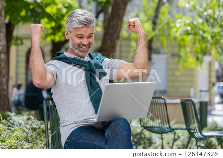 Mature man using laptop computer celebrating win good message news lottery jackpot casino victory Mature man using laptop computer celebrating win good message news lottery jackpot casino victory 126147326