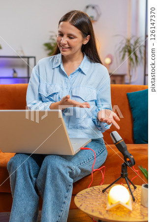 Happy blogger woman recording podcast at desk, giving workshop webinar speaking at microphone laptop Happy blogger woman recording podcast at desk, giving workshop webinar speaking at microphone laptop 126147370