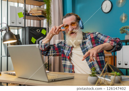 Happy senior man listening music through wireless headphones relaxing taking a break with laptop Happy senior man listening music through wireless headphones relaxing taking a break with laptop 126147402