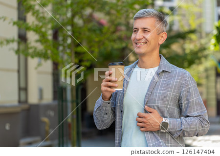 Happy mature Caucasian man enjoying drinking morning coffee hot drink and smiling on city street 126147404