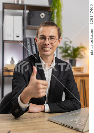 Smiling young Caucasian businessman freelancer showing double thumbs up sitting at home office desk Smiling young Caucasian businessman freelancer showing double thumbs up sitting at home office desk 126147469