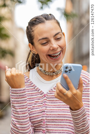 Young woman use mobile smartphone celebrating win good message news outdoors on urban city street 126147470
