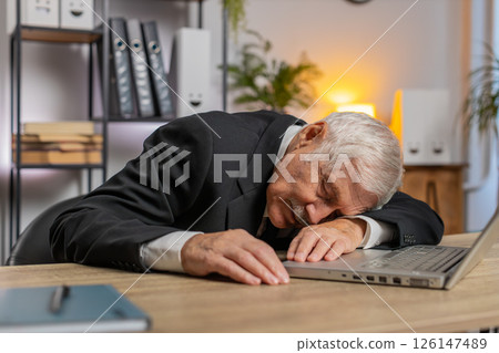 Bored sleepy senior businessman working on laptop leaning on hand falling asleep at office desk Bored sleepy senior businessman working on laptop leaning on hand falling asleep at office desk 126147489
