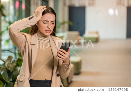 Young businesswoman using smartphone becomes shocked sudden lottery results in office hotel lobby 126147498