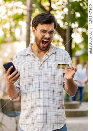 Angry Indian man trying to pay online shopping with smartphone blocked credit card on city street 126147500