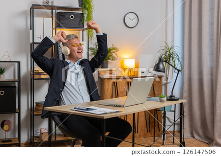 Happy young businessman wearing sunglasses and wireless headphones enjoy music at home office desk Happy young businessman wearing sunglasses and wireless headphones enjoy music at home office desk 126147506