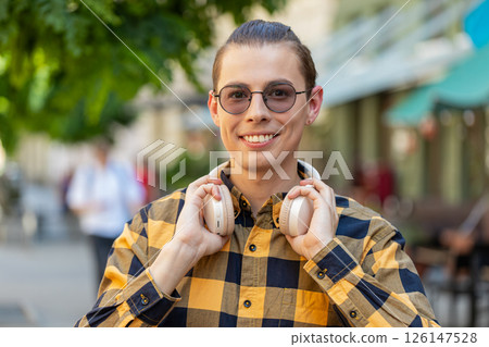 Happy smiling man listening music taking off wireless headphones looking at camera on city street 126147528