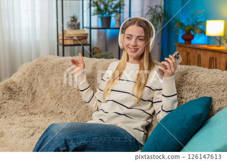 Caucasian woman enjoying relaxing on sofa listening to music with headphones holding smartphone 126147613