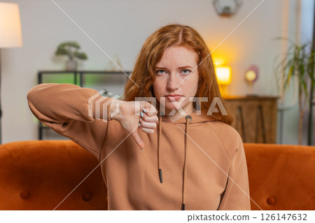 Upset woman showing thumb down sign gesture, expressing discontent sitting on sofa couch at home 126147632