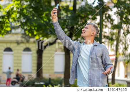 Mature male tourist trying to catch a communication signal and Internet on smartphone in city street Mature male tourist trying to catch a communication signal and Internet on smartphone in city street 126147635