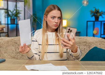 Caucasian woman frustrated with bill errors at home on table, checking smartphone, blocked payment Caucasian woman frustrated with bill errors at home on table, checking smartphone, blocked payment 126147682