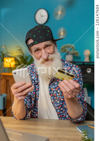 Happy senior man using bank credit card and laptop for online shopping payments at home office 126147684