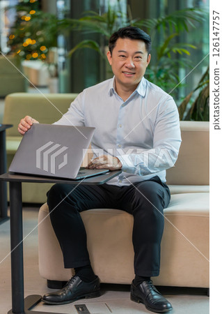 Portrait of smiling young businessman closing laptop computer after finishing work at hotel lobby Portrait of smiling young businessman closing laptop computer after finishing work at hotel lobby 126147757