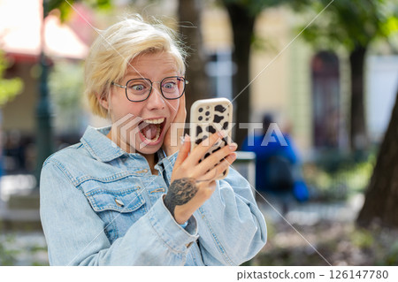 Happy Caucasian blonde woman using smartphone celebrating win good message news on city town street Happy Caucasian blonde woman using smartphone celebrating win good message news on city town street 126147780