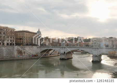 Scenic view of Ponte Sant Angelo bridge over Tiber River in Rome during daytime with reflections on water and classical architecture under soft sky. High quality photo 126148185